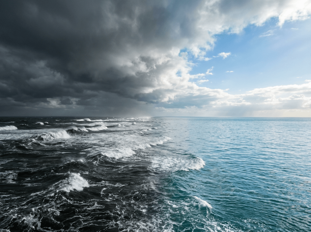 Ocean waves under dark storm clouds on the left and clear blue sky on the right